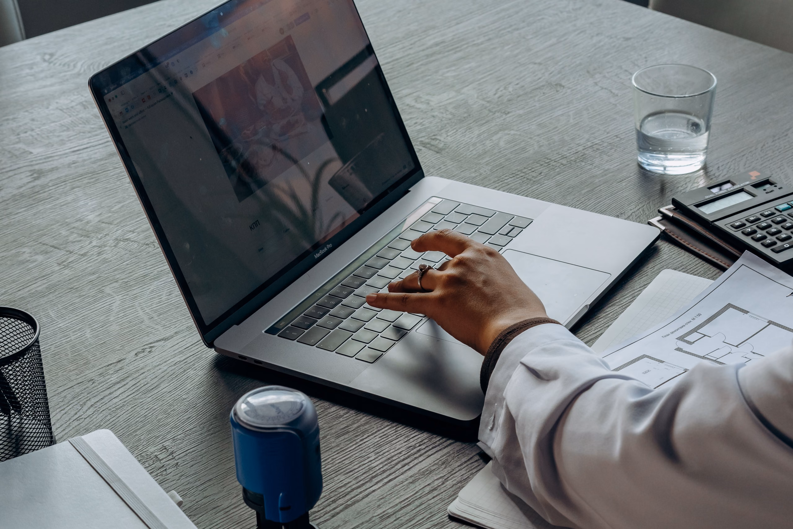 Een laptop op een bureau met een notarisstempel, een grondplan en een rekenmachine ernaast