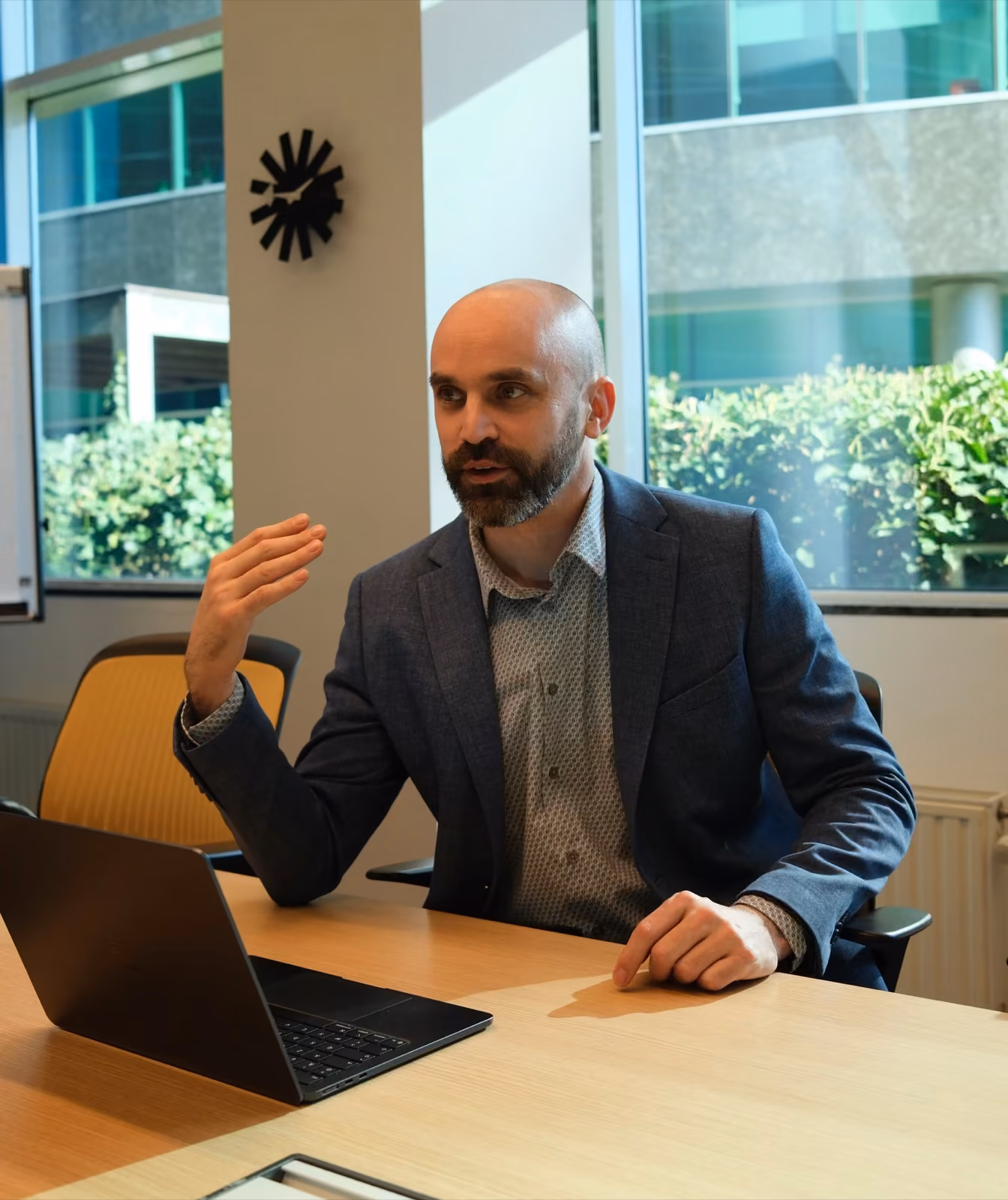 Quinten van Ulvio legt iets uit tijdens een overleg aan de vergadertafel, met een laptop voor zich.